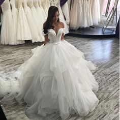 a woman in a white wedding dress is looking down at her gowns on display