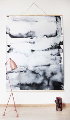 a black and white painting hanging on a wall with a pink lamp next to it