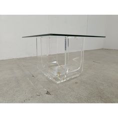 a clear glass table sitting on top of a cement floor next to a white wall