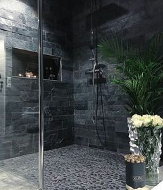 a bathroom with black tile and white flowers in the vase on the shower stall door