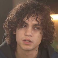 a close up of a person with curly hair and a black jacket in the background