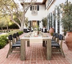 an outdoor dining table and chairs in front of a white house with red brick walkway