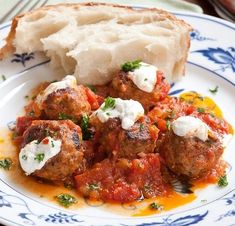 meatballs with tomato sauce and sour cream on a blue and white plate next to bread