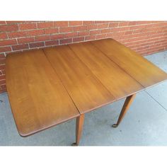 a wooden table sitting in front of a brick wall next to a sidewalk with no one on it