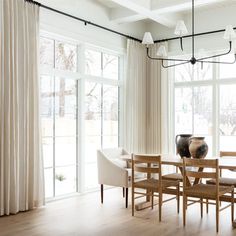 a dining room table with chairs and a vase on top of it in front of large windows