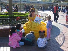 several children are sitting on the ground near a statue of a woman in a yellow dress