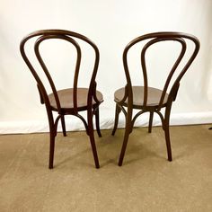 two wooden chairs sitting next to each other on a carpeted floor in front of a white wall