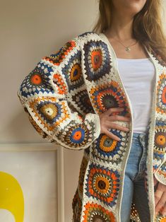 a woman is wearing a crocheted cardigan sweater and denim shorts with her hands on her hips