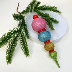 a christmas ornament hanging from a tree branch with glitter balls and ornaments around it