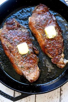 two pieces of meat in a skillet with butter on them and some seasoning