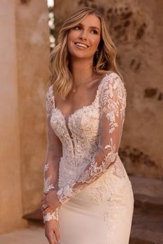 a woman wearing a wedding dress with long sleeves and sheer lace on the top, smiling