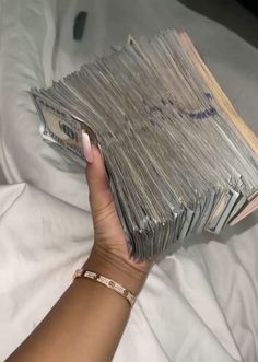 a woman is holding stacks of money in her hand on top of a white sheet