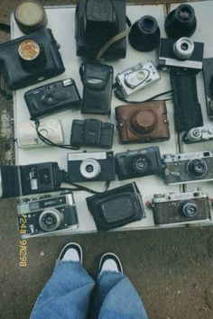 a person standing next to a bunch of old camera's on the ground with their feet up