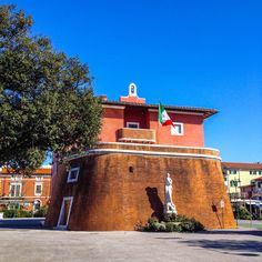 a red building with a flag on top and a statue in the foreground next to it