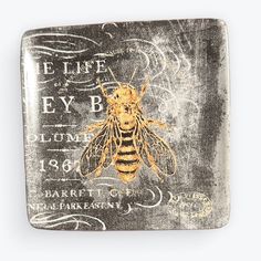 a square metal plaque with a bee on it's side and words written in gold