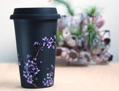 a black coffee cup with purple flowers painted on it