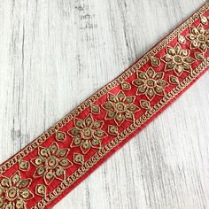 a red ribbon with gold flowers and beads on it sitting on a white wooden surface