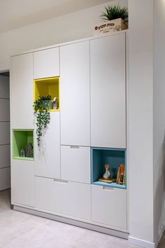 a white cabinet with green and yellow shelves next to a wall mounted planter in the corner