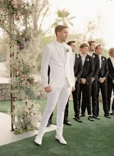 a man in a white suit standing next to a group of men wearing tuxedos