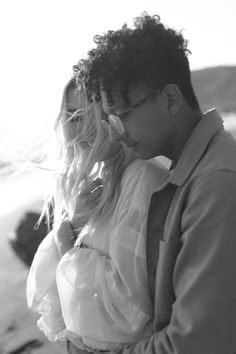 a man and woman standing next to each other in front of the ocean with their arms around each other