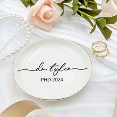 two wedding rings are sitting on a plate next to some pink roses and pearl necklaces