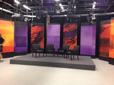 two people are walking past three large television screens with purple and orange designs on them