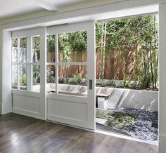 an empty room with sliding glass doors and wood flooring in the center, looking out onto a garden