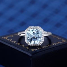 an engagement ring with a blue topazte surrounded by diamonds on a black box