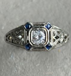 an antique diamond and blue sapphire ring with filigrees on the sides, set in white gold