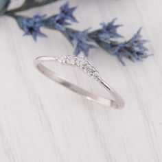 a white gold ring with three diamonds on it, sitting next to blue flower stems