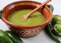 a brown bowl filled with green soup next to some vegetables and a wooden utensil