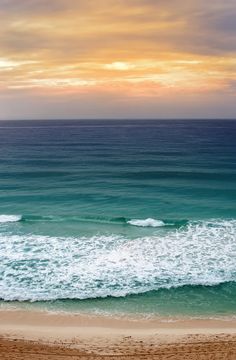 an ocean view with waves crashing on the shore and people walking in the sand at sunset