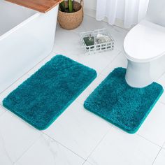 two bathroom rugs on the floor in front of a toilet and bathtub with a plant next to it