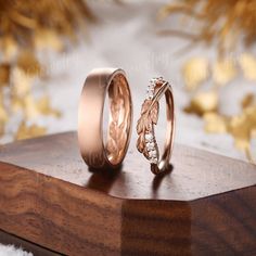 two wedding bands with leaves on them sitting on top of a wooden stand next to each other