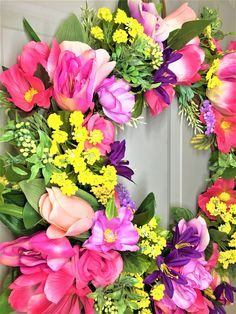 a wreath with pink, yellow and purple flowers on the front door is decorated with greenery