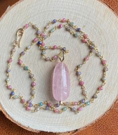 "This soft pastel colored multi Sapphire necklace featuring a stunning centerpiece, a large peachy pink Morganite pendant, captures the essence of the season, radiating femininity. The large, smooth polished natural pink Morganite pendant measures 2.2 x 1.1 cm. This alluring gemstone is suspended from a 19.5\" (50 cm) long multicolor Sapphire rosary chain, fastened by a hand forged 14k gold filled hook clasp. The sparkly multi Sapphire rosary chain boasts a luxurious 22k gold vermeil finish. The Feminine Pink Pendant Jewelry, Feminine Pink Rose Quartz Jewelry, Pink Morganite Jewelry With Gemstone Accents, Pink Morganite Gemstone Jewelry, Pink Gemstone Jewelry For Jewelry Making, Feminine Multicolor Jewelry For Gifts, Pink Gold Gemstone Pendant Necklace, Pink Gold Pendant Necklace With Gemstone, Pink Opal Gemstone Pendant Necklace