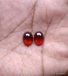 two red glass balls sitting on the palm of someone's hand in front of them