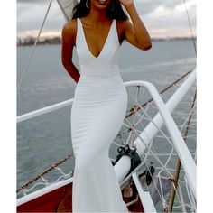 a woman in a white dress standing on the deck of a boat looking at the camera