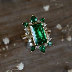 an emerald and diamond ring sitting on top of a wooden table next to dried flowers