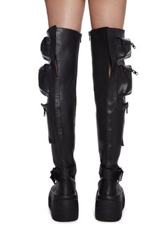 These thigh high combat boots have a vegan leather construction, heeled platform soles, zippered pockets on the sides, buckle strap details, adjustable lace-ups, and side zip closures. Alternative Faux Leather Platform Boots For Concert, Edgy Faux Leather Boots For Streetwear, Alternative Style Faux Leather Boots For Concert, Alternative Style Faux Leather Platform Boots For Concerts, Alternative Style Faux Leather Moto Boots, Gothic Knee-high Combat Boots For Concerts, Knee-high Faux Leather Punk Platform Boots, Edgy Knee-high Platform Combat Boots, Black Alternative Style Knee-high Boots For Concerts