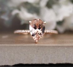 a pink diamond ring sitting on top of a wooden table next to white flower petals