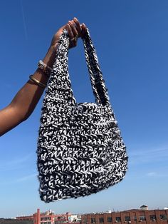 a person holding up a black and white bag in front of a blue sky with buildings