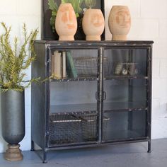 a black cabinet with some vases on top of it next to a plant and a mirror