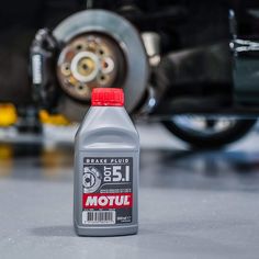 a bottle of motor oil sitting on the ground next to a car tire and brake fluid