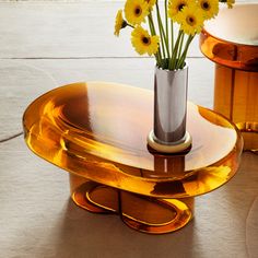a vase with yellow flowers sitting on top of a glass table next to another one