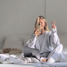 a woman sitting on a bed while holding a cell phone and looking at her laptop