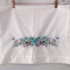 an embroidered white cloth hanging on a clothes line with flowers and leaves painted on it