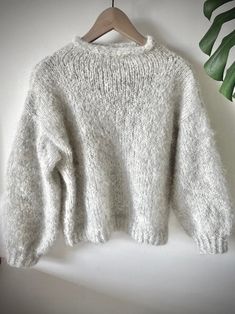 a white sweater hanging on a wooden hanger next to a green leafy plant