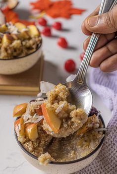 a person is holding a spoon over a bowl of fruit and oatmeal