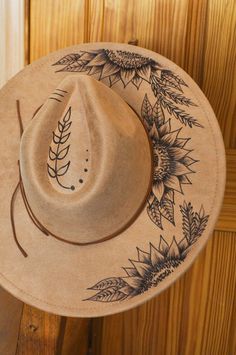 Step into the sunshine with this one-of-a-kind hand-burned sunflower suede fedora! Perfect for nature lovers and bohemian souls, this wide-brim hat features intricate sunflower and leaf designs, individually burned into the soft suede for a rustic yet refined look. Ideal for festival fashion, outdoor adventures, or adding a touch of botanical charm to your everyday wardrobe. Each hat is carefully crafted using freehand pyrography, ensuring that no two pieces are exactly alike. Whether you're a fan of Western-style fedoras, or you just want to make a bold statement, this unique piece will elevate your look with a blend of artistry and earthy elegance. Key Features: - Hand-burned sunflower and leaf designs - Crafted from high-quality tan suede - Wide-brim fedora for sun protection and style Burning Hats, Western Hat Styles, Burnt Hat, Burnt Hats, Western Inspired Outfits, Burned Hats, Boho Hats, Hat Burning, Nature Inspired Accessories